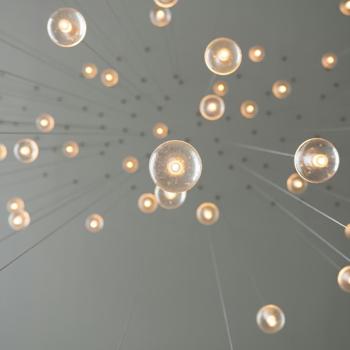 Photo of lightbulbs hanging from a ceiling, looking like nodes of light in a network, resembling a conception of brain neurons.