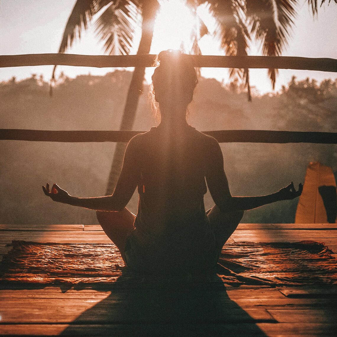 Photo of a woman meditating on a deck in the sunset, warm glow.
